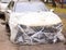 A broken car color silver, wrapped in a plastic coating. The car is covered with polyethylene after the accident. It is very debt.