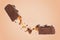 Broken chocolate bar with yummy caramel in air on pale brown background