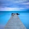 Broken concrete pier or jetty and rocks on a blue sea. Hills on background