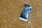 Broken crashed smartphone is lying in the water. Phone in the sandy beach