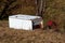 Broken destroyed large partially rusted white refrigerator dumped in nature as illegal garbage next to plastic beer crate