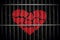 Broken heart paper cutout behind metal bars in black background.
