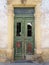 Broken old double green doors with rusty letterbox in an abandoned derelict house with broken windows and faded peeling paint