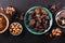 Broken pieces of chocolate in a vintage bowl and ingredients for making chocolate sweets on a dark textured background, top view.