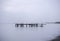 Broken pier posts in calm tranquil water, misty foggy blue background seascape