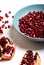 Broken pomegranate and pomegranate seeds in blue plate. Garnet seeds. White background. Closeup.