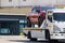 Broken red pickup car loaded onto white towing truck in public area for transportation to garage