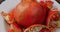 Broken ripe red pomegranate fruit on a white plate rotates in a circle