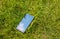 Broken smartphone lying in the green grass lawn outdoors. Damaged screen from the accidental fall. Modern technologies and nature