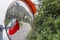 Broken spherical road safety mirror with cracks and red plastic on a background of green foliage. Reflected asphalt road