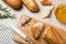 Broken tasty baguette, knife and rosemary on white wooden table, flat lay