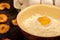 A broken white chicken egg in a bowl with wheat flour, dried apple chips and several whole eggs in a tray made of white cardboard