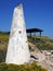 Broken white conical concrete structure next to a shelter on the coastal cliffs surrounded by yellow spring flowers and a bright