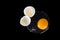 Broken white raw egg, yellow round yolk, two cracked halves of eggshell on black background isolated close up top view