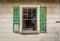 Broken window with green shutters on old rustic abandoned barn surrounded by bright fall foliage