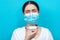 Bronchial asthma. Blurry portrait of a woman in a medical mask holding an inhaler in front of her. Blue background