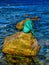 Bronze mermaid sculpture called Sirenella di L`Isula Rossa sitting on a rock in the Mediterranean Sea