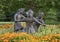 Bronze statue of a boy and two girls happily dancing in a circle in a bed of orange flowers in Irving, Texas.