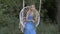 A brooding young blonde girl swings on a white hanging swing in a blue dress with a bouquet of yellow wildflowers at the