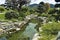 A brook flows between the rocky banks. Around green tropical vegetation.