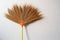 The broom is made from grass and has plastic handles rests against the white concrete wall and soft sunlight.