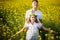 Brother catches sister in dress and Ukrainian wreath that falls into his hands in rapeseed field