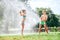 Brother and sister play together with watering hose in garden