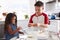 Brother and sister preparing cake mixture together at the kitchen table, waist up