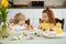 Brother and sister are sitting at the kitchen table and painting Easter eggs. Children getting ready for Easter holidays.