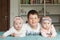 Brother and sisters lie on the bed and smiling. Brother embraced his little twin sisters. They are very happy with each other