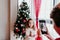 brother taking a picture of his sister with mobile phone at home. Girl standing by the christmas tree. Family time. Christmas