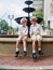 Brothers with bowties and hats sitting on a fountain and looking at each other in a park