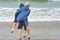 Brothers playing piggyback at the edge of waves on coast