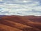 Brown autumn Caucasian hills under the sky in gradually dissipating clouds. Smooth mountains as if covered with a carpet