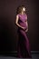 On  brown background is a young pregnant woman, a full-length photograph, looking to the side, beautiful makeup and hairstyle, a