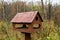 Brown bird house feeding trough with a sloping roof on a spring forest background