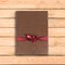 Brown book gift. With red ribbon and bow. On a wooden table