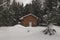 Brown cabin in field of pristine snow with evergreens in background