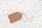 Brown cardboard label, tag with slim rope cord on white knitted background