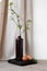 Brown ceramic vase with tree branch, natural brown eggs on table with neutral beige linen curtain and white wall