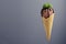 Brown creamy ice cream scoop in waffle cone with chocolate sauce, green mint leaf on grey background.