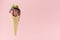 Brown creamy ice cream scoop in waffle cone with chocolate sauce, green mint leaf on pink background.