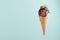 Brown creamy ice cream scoop in waffle cone with chocolate sauce, green mint leaf on soft light green background.