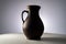 Brown earthenware jug with a handle in a dark studio. An old jar from clay standing on a white table isolated on a gray