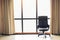 Brown executive leather chair in empty office space with large window and drape