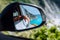 Brown female hand in the car side view mirror. Blue mediterranean sea and white rocks in background