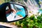 Brown female hand in the car side view mirror. Blue mediterranean sea and white rocks in background