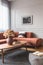 Brown flowers in pottery vase on stylish coffee table in chic living room interior with black and white poster on the grey wall