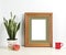 Brown frame mockup with plant pot, mug and apple on wooden shelf