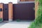 Brown gate and part of a fence made of metal and bricks outside in green vegetation